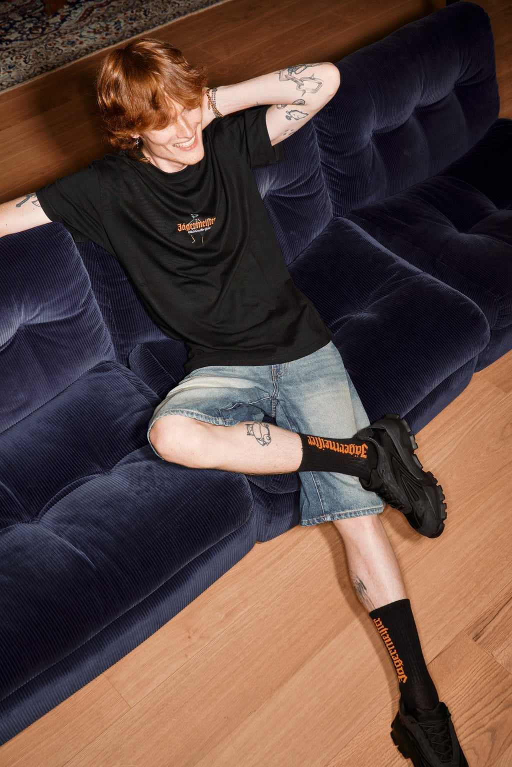 Pessoa sentada num sofá azul com meias pretas e branding Jägermeister visível.