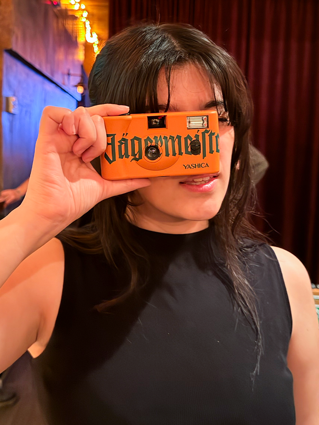 Person holding an orange camera with 'Jägermeister' branding in front of their face.