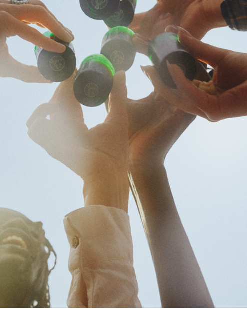 Multiple hands holding green Jägermeister shot glasses against a clear sky