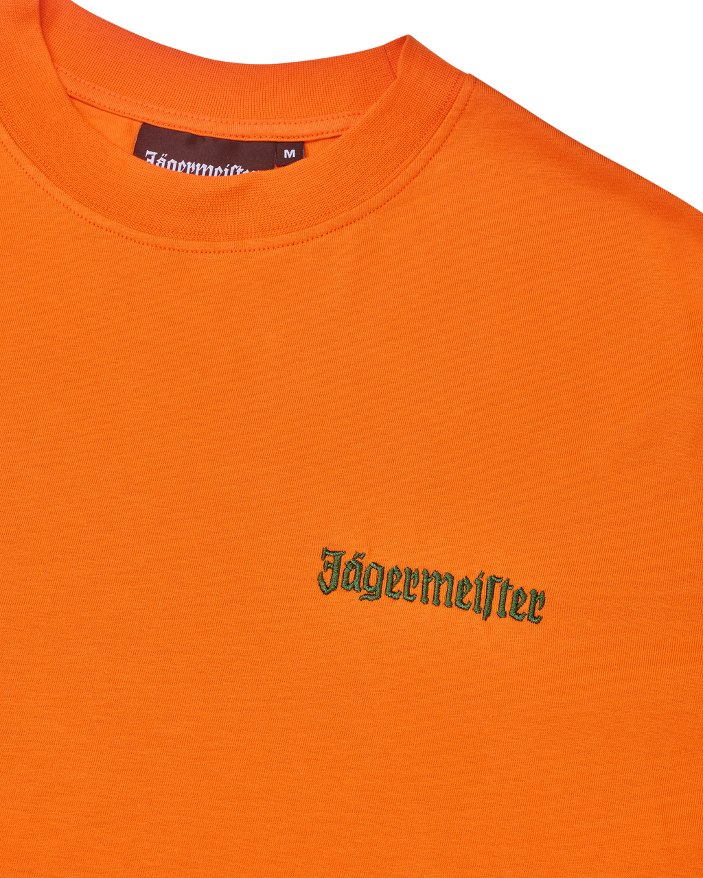 T-shirt laranja com logótipo Jägermeister verde no peito.