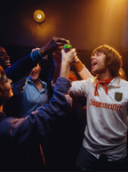 Grupo de pessoas a celebrar com uma pessoa a usar uma t-shirt Jägermeister numa sala pouco iluminada.